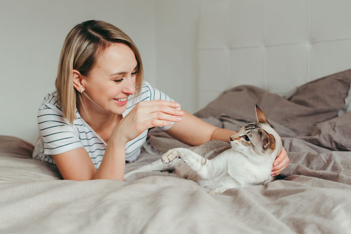 Woman pats cat on bed 